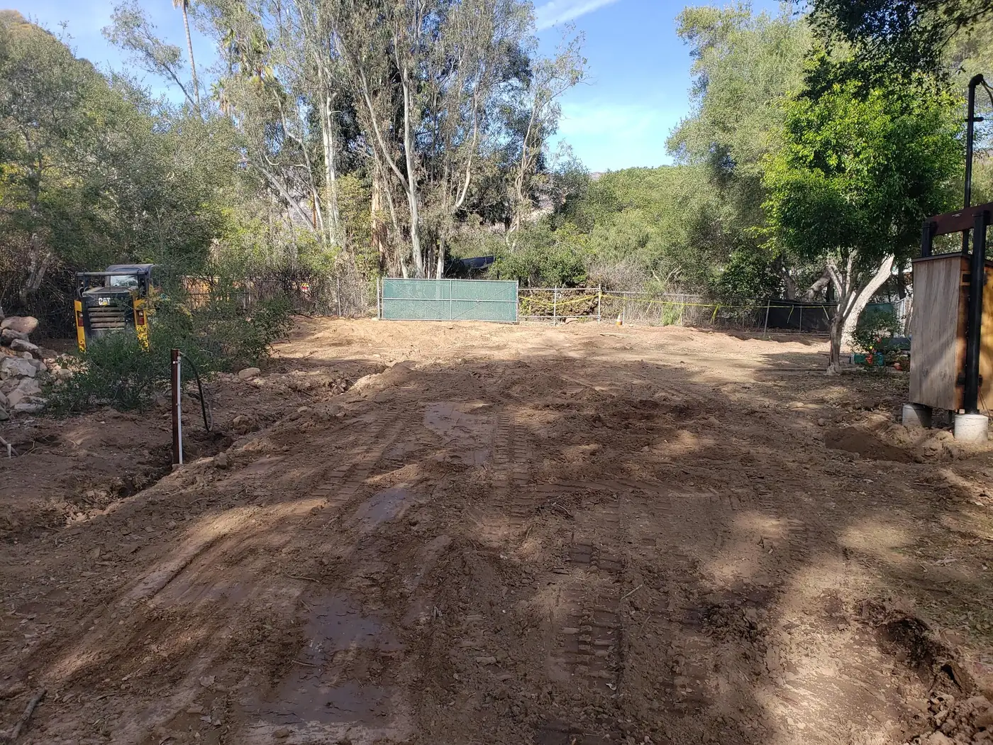 Freshly graded backyard with machine tracks in the bare dirt and a compact loader parked at the edge